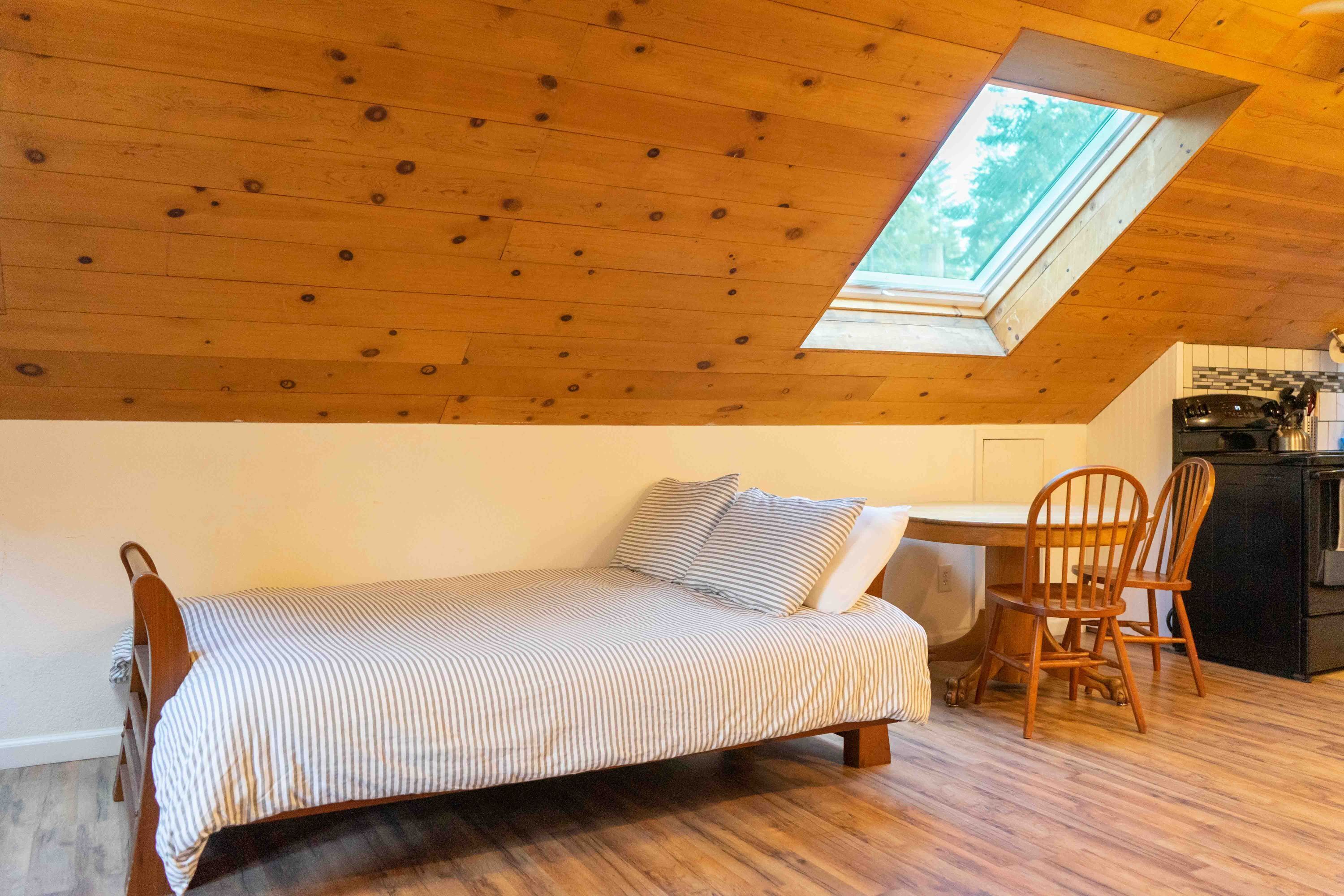 A small, cozy room with a sloped ceiling, a single bed, a wooden table, and two chairs.