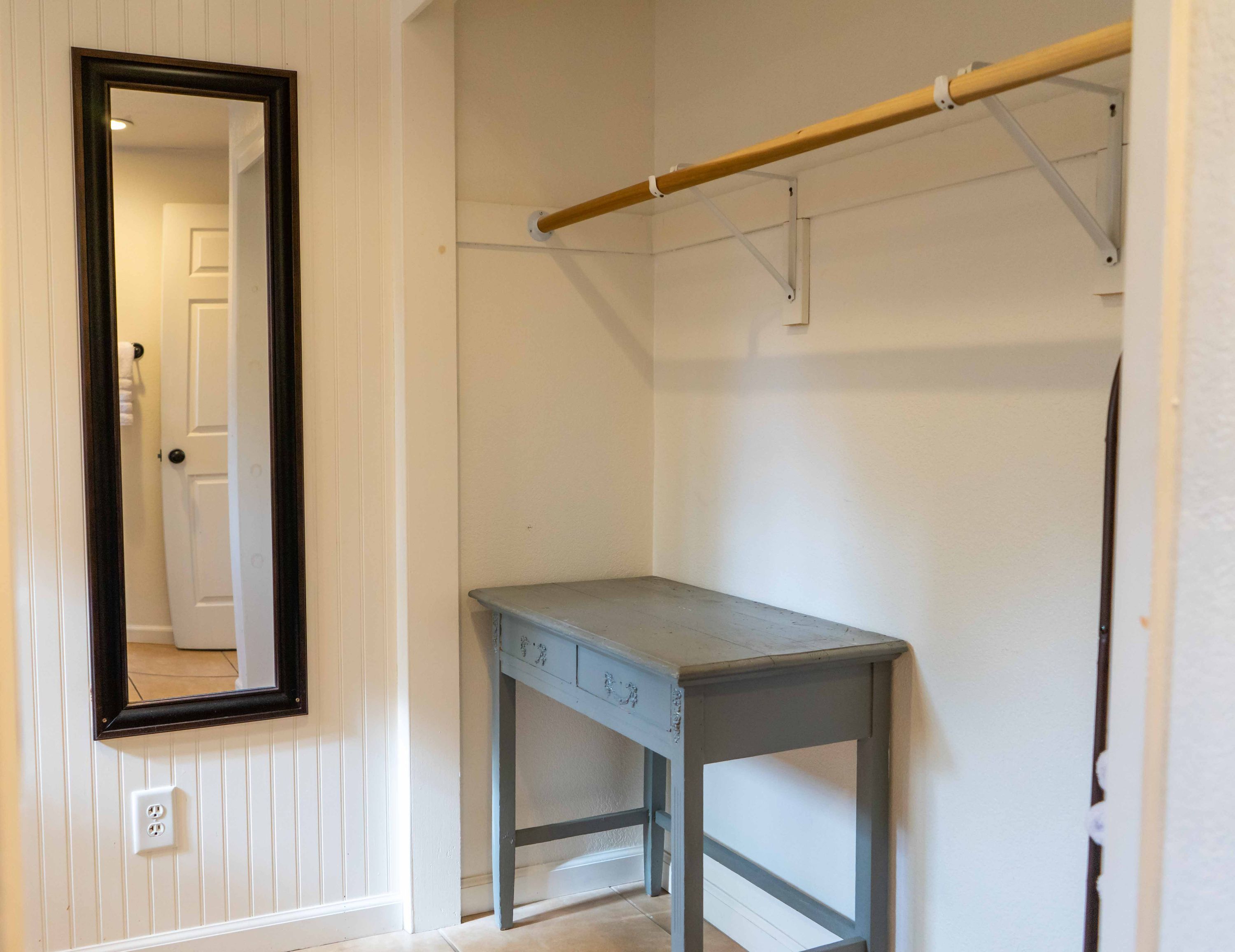 A room with a wooden table, a mirror, and a clothes rack.