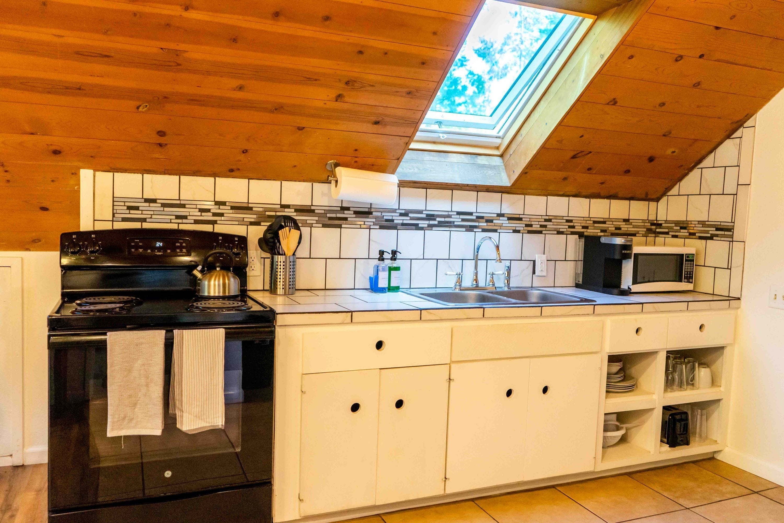 A kitchen with a skylight, a stove, a microwave, and a sink.