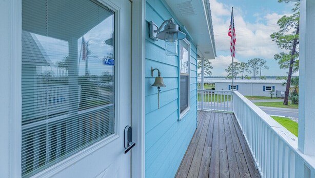 A porch with a wooden deck, a white door, and a blue exterior wall. - Bear Point Bayview Cottage – Bay Views, Marina Walk (Orange Beach)
