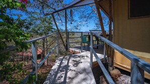 Une terrasse en bois avec des rampes en métal, un chemin en béton et un bâtiment jaune en arrière-plan.