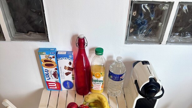 A breakfast table with croissants, apples, bananas, juice, and a red bottle. - Appartement Cosy - Chartreux (Marseille)
