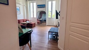 A spacious living area with a wooden floor, a green table, a red sofa, and a painting on the wall. - Appartement Cosy - Chartreux (Marseille)
