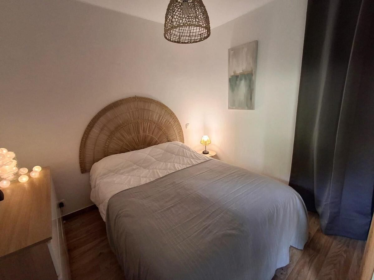 Un dormitorio con cama, lámpara de noche y una lámpara fijada a la pared.