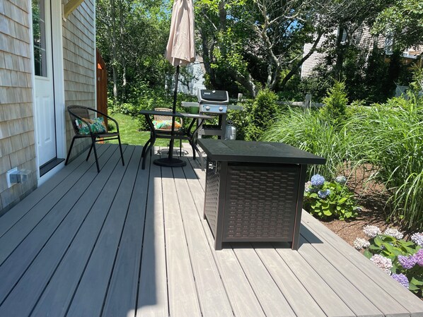 Eine Holzterrasse mit Tisch, Stühlen, einem Grill und einem Korb.