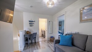 A modern living room with a grey sofa, a coffee table, and a dining area with a table and chairs. -  Edgartown cottage in a garden setting.  New and near bike path in Katama (Edgartown)