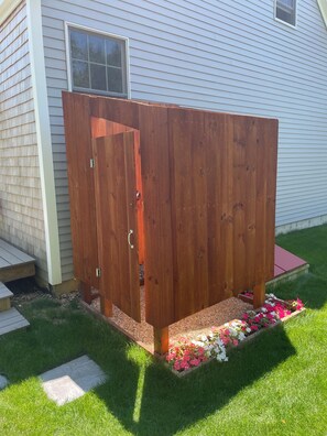 A wooden fence with a door, a small garden area with flowers, and a house in the background.