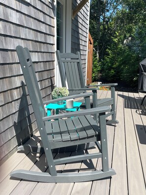 A deck with a wooden table and two rocking chairs.