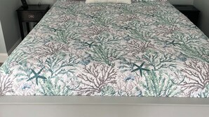 A bed with a coastal life themed bedspread, a bedside table with a phone, and a wall-mounted lamp. -  Edgartown cottage in a garden setting.  New and near bike path in Katama (Edgartown)