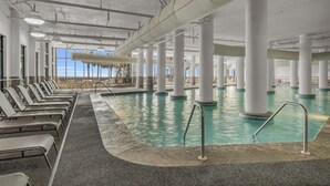 An indoor swimming pool with multiple columns, lounge chairs, and a view of the sky. - 1605 3bd Oasis Beach Paradise - OasisAtOrangeBeach (Orange Beach)