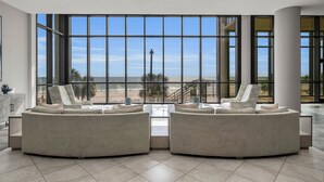 A spacious living area with a large window overlooking a beach and a cross, featuring a modern sofa and a coffee table. - 1605 3bd Oasis Beach Paradise - OasisAtOrangeBeach (Orange Beach)