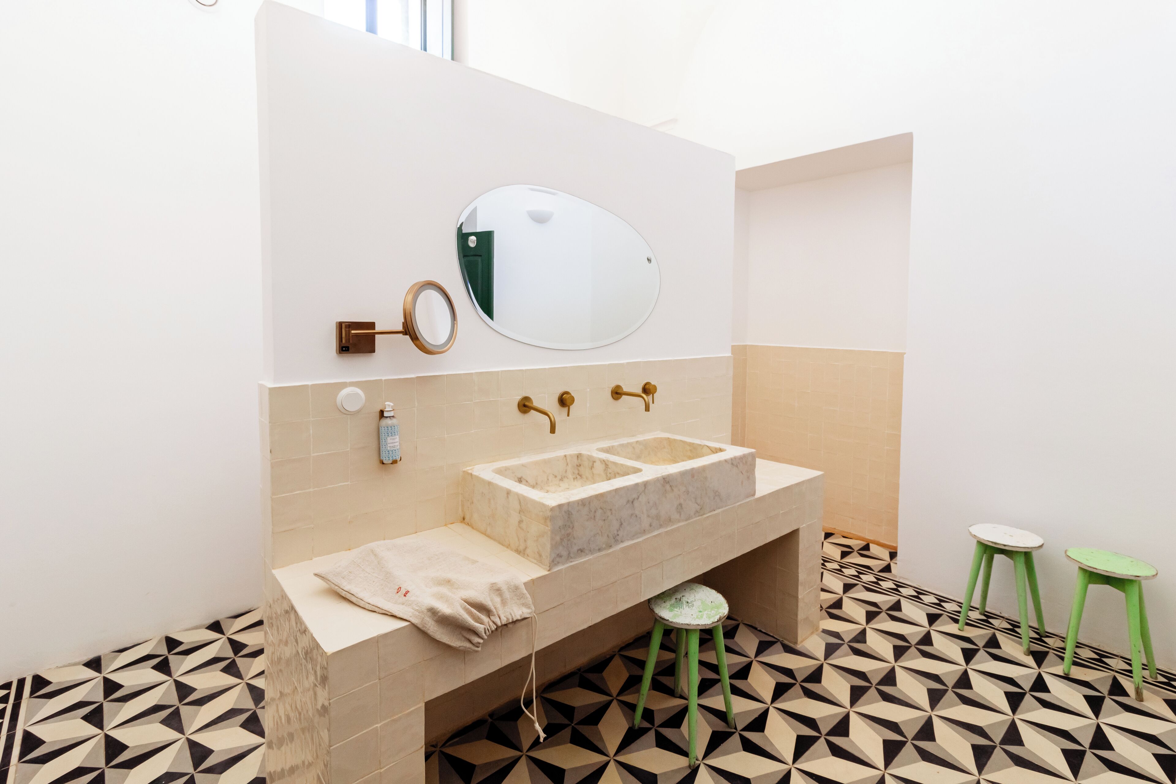 Un baño con lavamanos de mármol, un espejo y una toalla en la encimera. Hay dos taburetes y un suelo estampado.