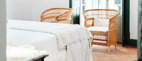 A bedroom with a bed, two wicker chairs, a television on the wall, and a green door leading outside.