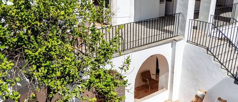 A white building with a swimming pool, a tree, and two lounge chairs.