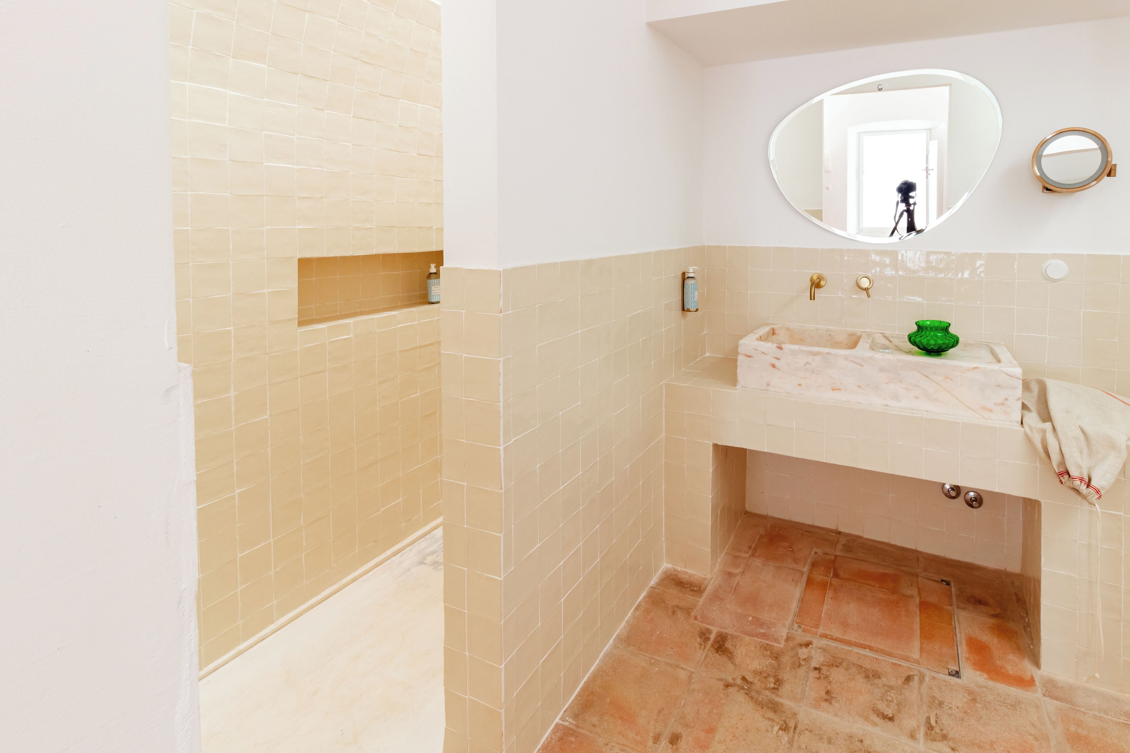 A bathroom with a beige tiled wall, a sink with a green vase, and a mirror above the sink.