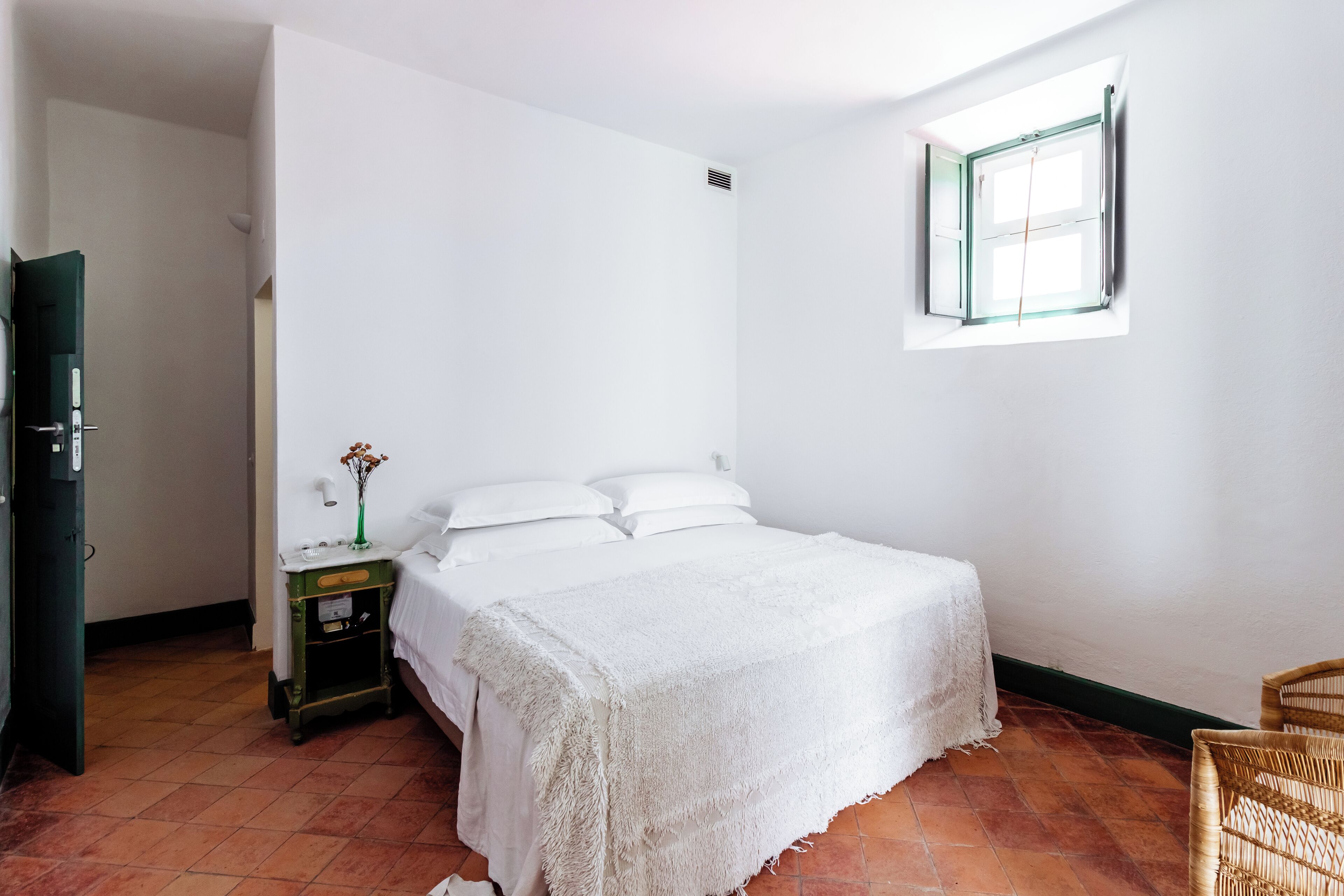 Ein Schlafzimmer mit einem Bett, einem Nachttisch, einem Fenster und einer Tür.
