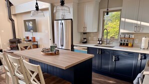 A modern kitchen with a central island, wooden chairs, a built-in stove, and a large window.