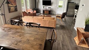 A spacious living area with a large wooden dining table, a sofa, and a TV.