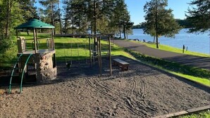 A park with a playground, a bench, and a gazebo near a lake.