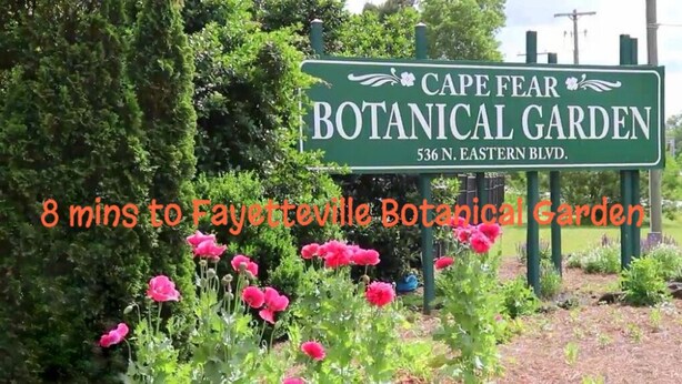 Schild für den Cape Fear Botanischen Garten mit der Aufschrift '8 Minuten bis zum Fayetteville Botanical Garden' und Blick auf rosafarbene Blüten.