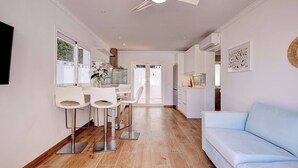 Une cuisine moderne avec des tabourets de bar blancs, un canapé bleu et un ventilateur de plafond.