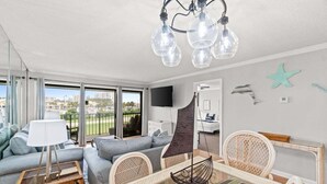 A modern living room with a sofa, chairs, a table, and a hanging light fixture. - Fall Deals + Snowbird Rates | Coastal Stay Near the Beach (Panama City Beach)