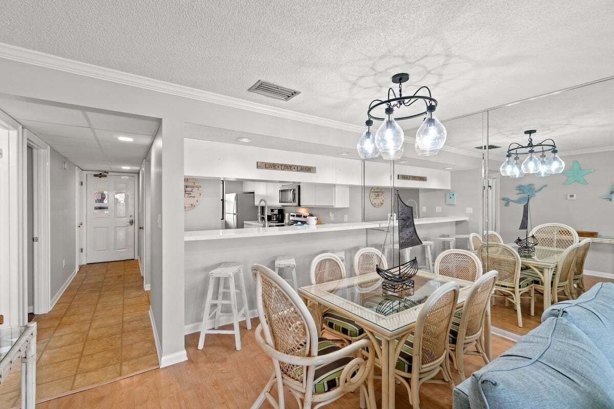 A modern kitchen with white cabinets, a central island, and a dining area with wicker chairs and a glass table.