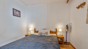 Un dormitorio con una cama individual, dos mesitas de noche con lámparas, un cabecero de madera, un cuadro enmarcado en la pared y suelo de madera.
