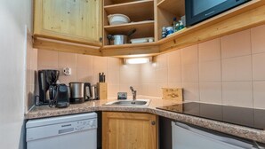 Una cocina compacta con armarios de madera, un lavamanos, lavavajillas, cafetera y microondas.