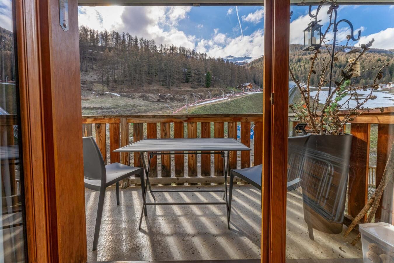Una terraza de madera con una mesa y sillas, con vista a un paisaje boscoso y un cielo despejado.
