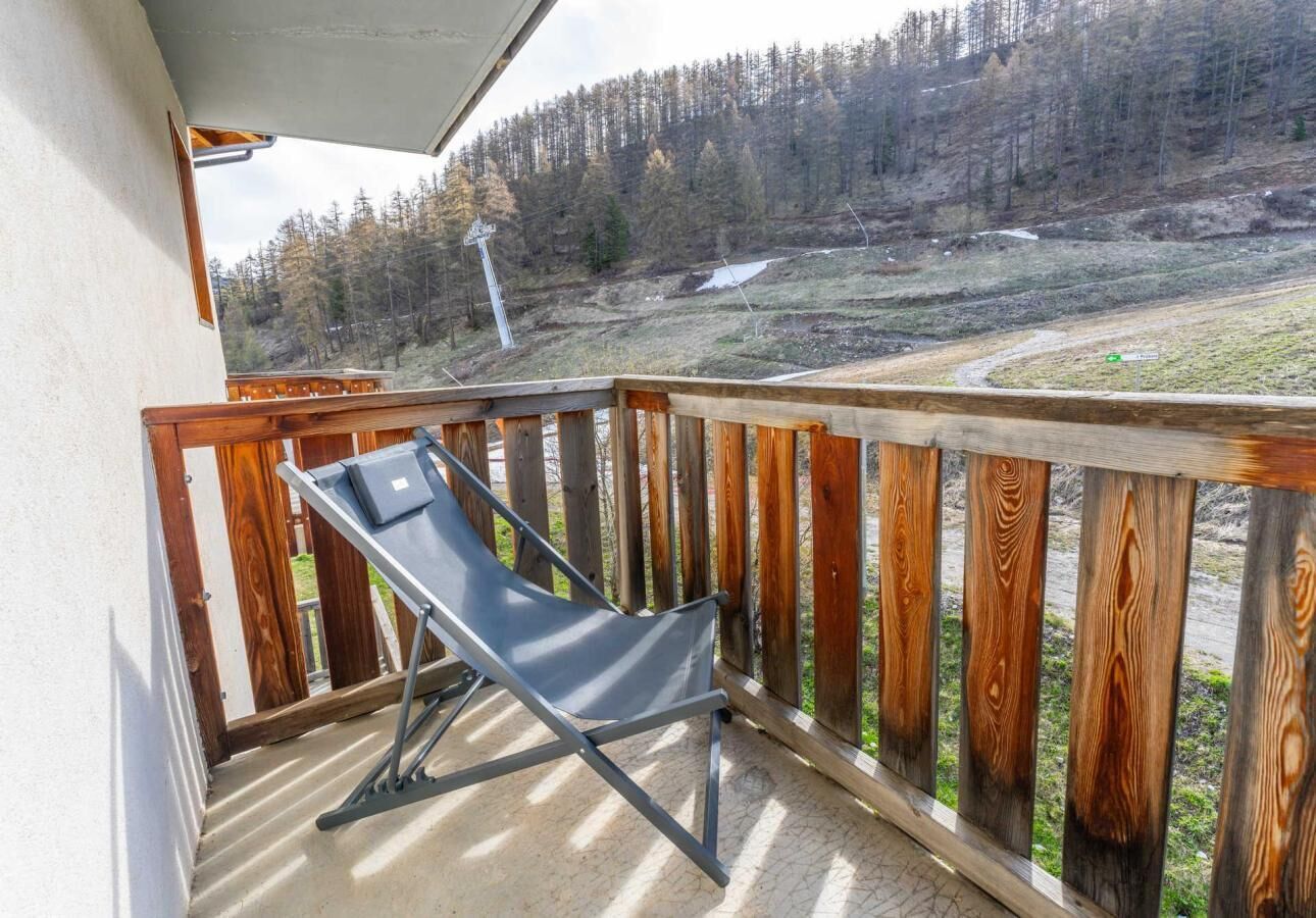 A balcony with a metal chair, wooden railing, and a view of a forested hillside.