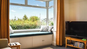 Un salón acogedor con un ventanal grande, un sofá, un televisor sobre un mueble de madera y una mesita con mandos a distancia.