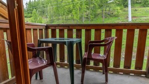Un balcon avec une table et deux chaises, donnant sur un espace verdoyant avec des arbres.