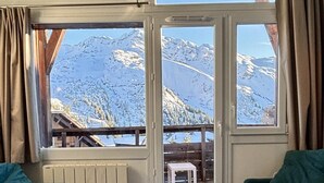 A cozy room with a wooden table, two green sofas, and a view of snow-covered mountains through large windows. - 10m from ski slopes, 5th floor, view mountain, balcony, tv, ski locker, 41m², Avoriaz (Avoriaz)