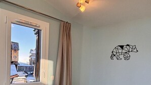 A dining area with a table set for four, white chairs, a window with curtains, and a wall-mounted light fixture. - 10m from ski slopes, 5th floor, view mountain, balcony, tv, ski locker, 41m², Avoriaz (Avoriaz)