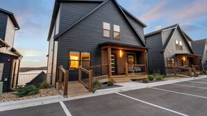 A modern two-story building with a dark exterior, a wooden deck, and a view of a body of water. - Golf Lodge Lake Views Hot Tub Rooftop Arcade (Hollister)