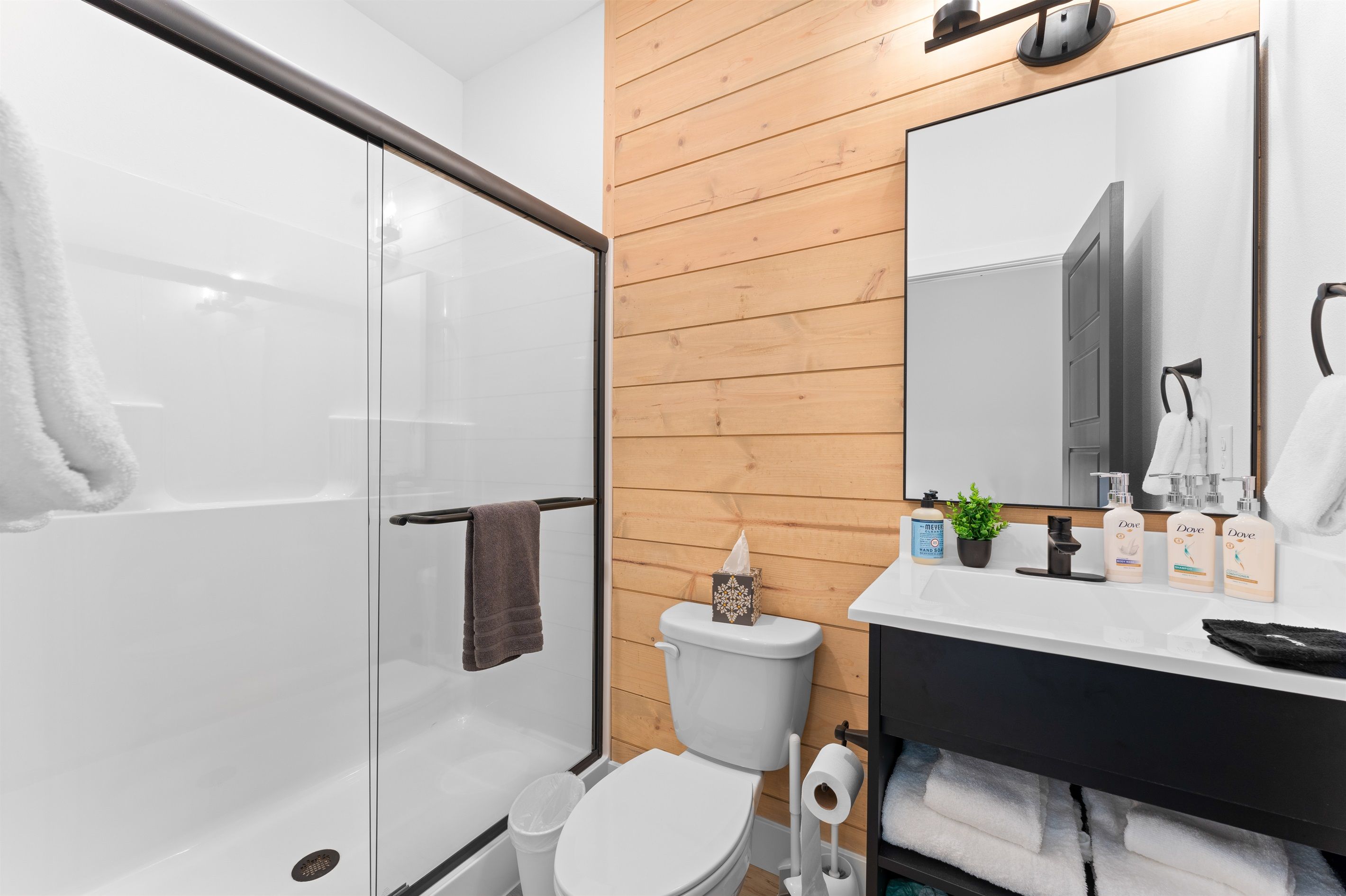 Een moderne badkamer met een glazen douchecabine, een wit toilet en een wandpaneel van hout.