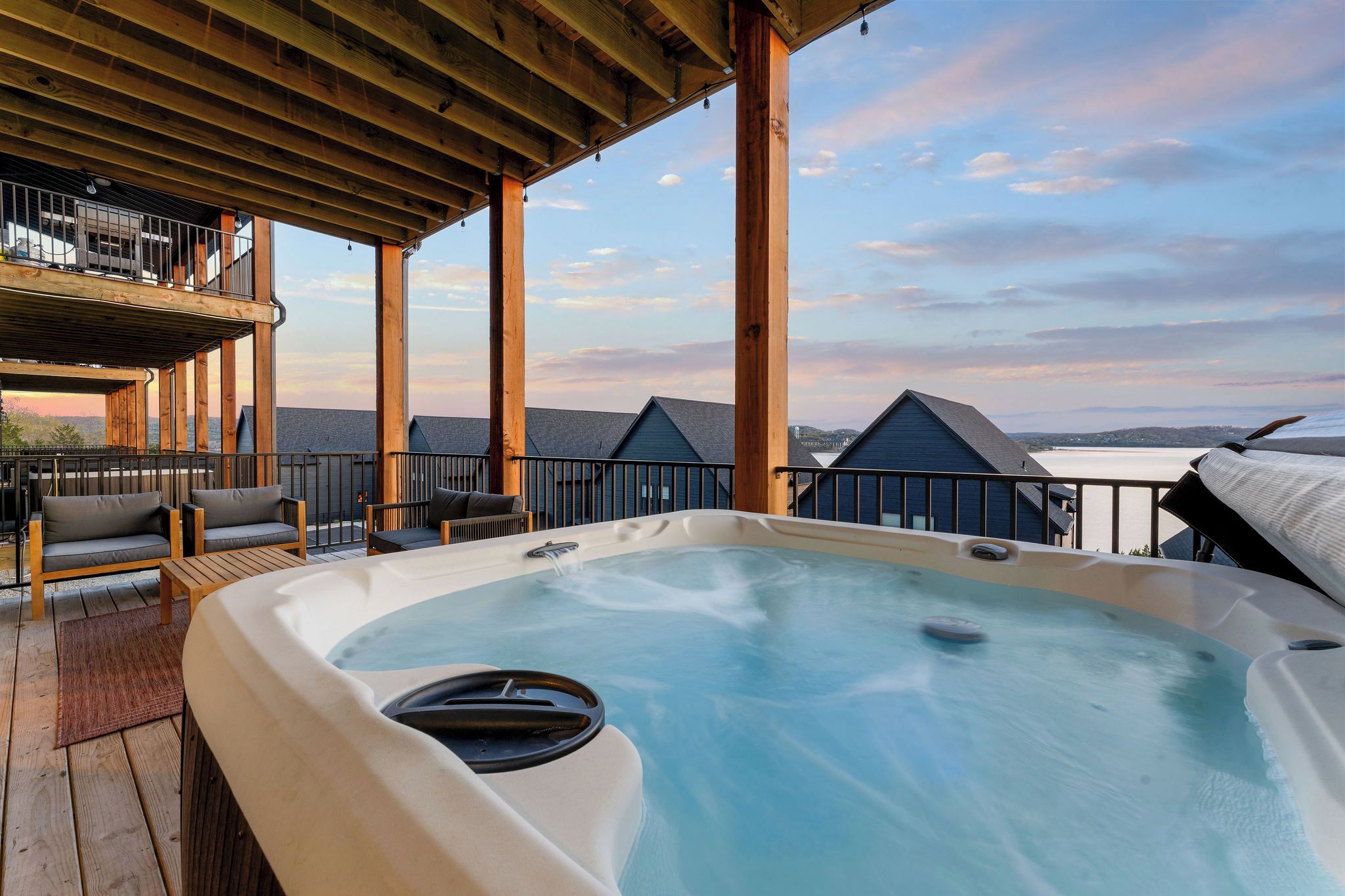 A hot tub on a wooden deck with a view of buildings and a body of water.