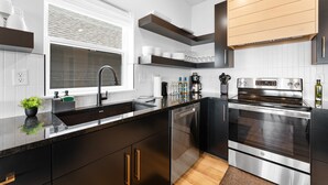 Une cuisine moderne avec des meubles de couleur noire, des appareils en acier inoxydable et une fenêtre équipée de stores.