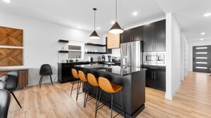 A modern kitchen with a central island, black cabinets, stainless steel appliances, and wooden flooring. - Branson GOAT: Golf Simulator Hot Tub Lake View Fun (Branson)