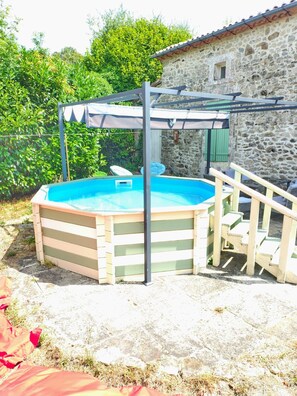 Ein Garten mit Schwimmbad, einer Pergola und einem Steinhaus.