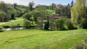 Paisaje rural con un río, campos verdes y un edificio pequeño.