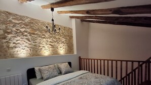 Un dormitorio con pared de piedra, cama con ropa de cama estampada, cabecero de madera y una araña.