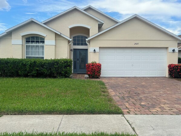 A two-story house with a beige exterior, a dark blue front door, and a white garage door. - Disney World Vacation Home (Kissimmee)