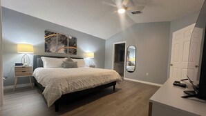 A bedroom with a bed, two bedside tables with lamps, a ceiling fan, a large mirror, and a door. - Disney World Vacation Home (Kissimmee)