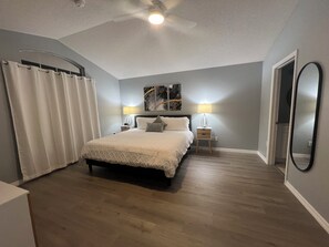 A bedroom with a bed, two bedside tables with lamps, a ceiling fan, and a large mirror on the wall. - Disney World Vacation Home (Kissimmee)