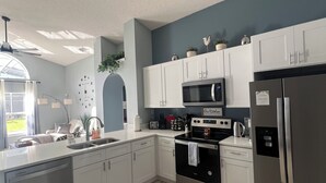 A modern kitchen with white cabinets, stainless steel appliances, and a tiled floor. - Disney World Vacation Home (Kissimmee)