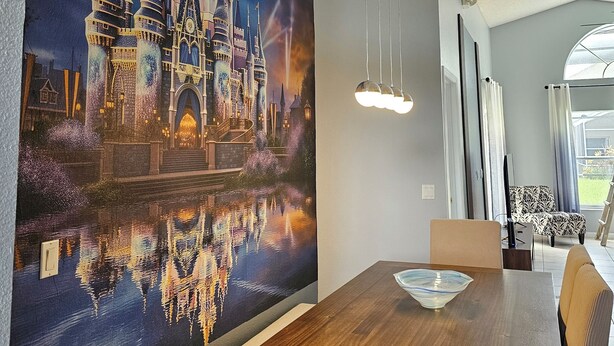 A dining area with a large mural of a castle, a wooden table, and modern lighting fixtures. - Disney World Vacation Home (Kissimmee)
