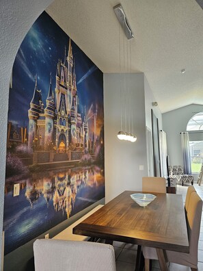 A dining area with a large mural of a castle, a wooden table, and modern lighting fixtures. - Disney World Vacation Home (Kissimmee)