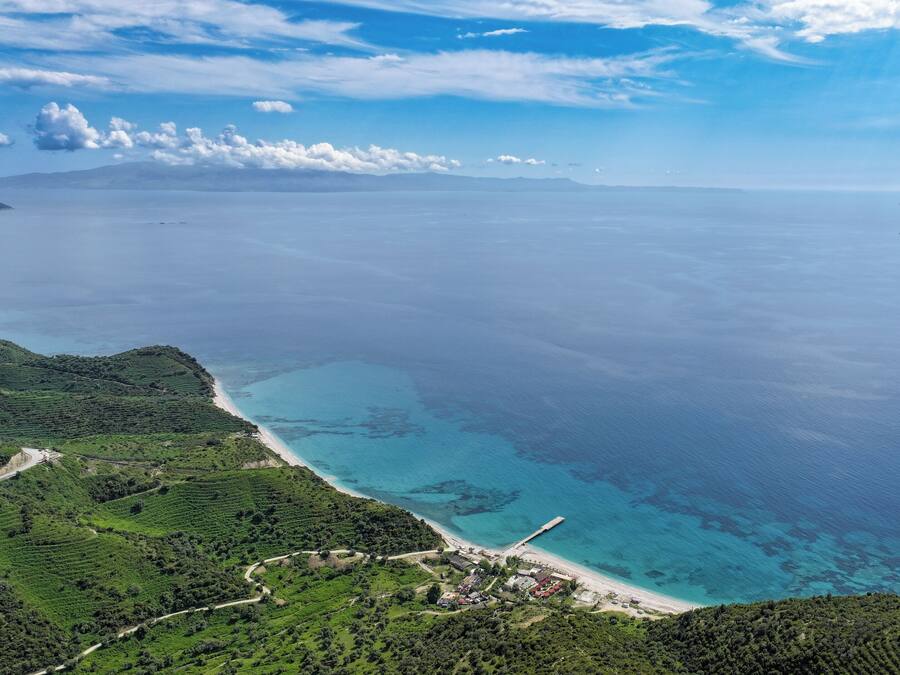 A coastal landscape with terraced fields, a beach, and a pier extending into the sea.